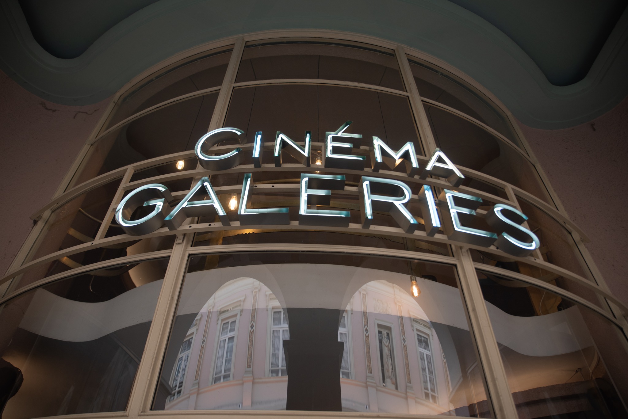 Neonový nápis „Cinéma Galeries“ na zaoblené fasádě budovy.